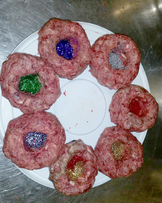 Seven meatballs on a plate. Each is filled with a unique colour of glitter. 